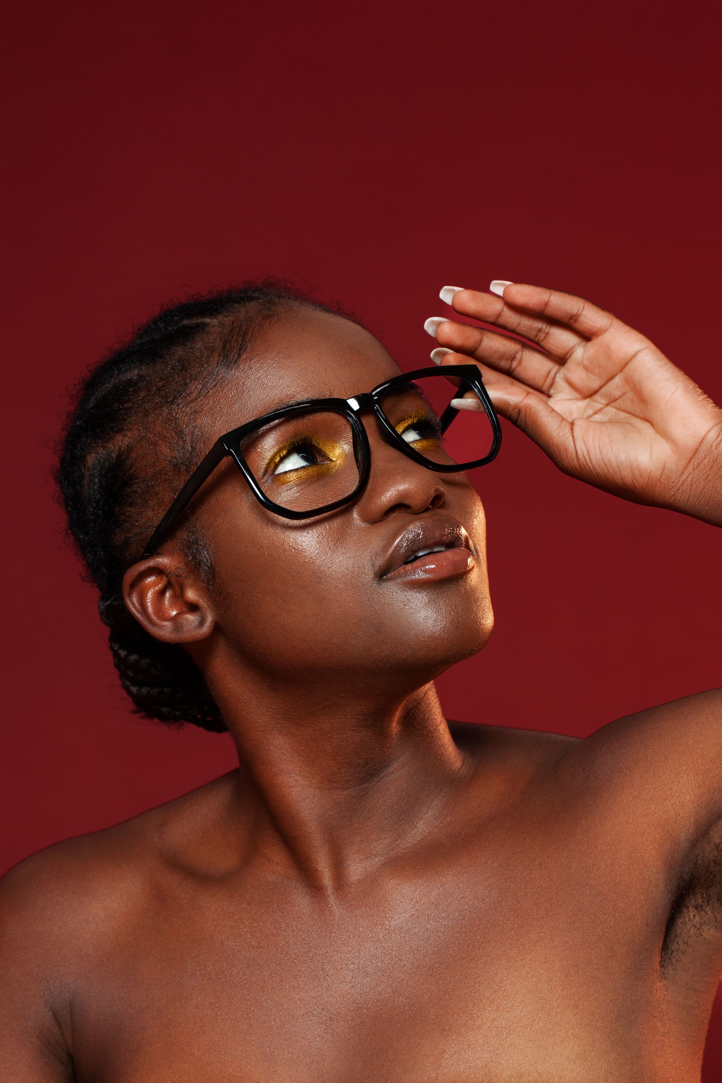 Before — editorial portrait of deep skin with glasses on red backdrop, showing pores, oil shine, and imperfections